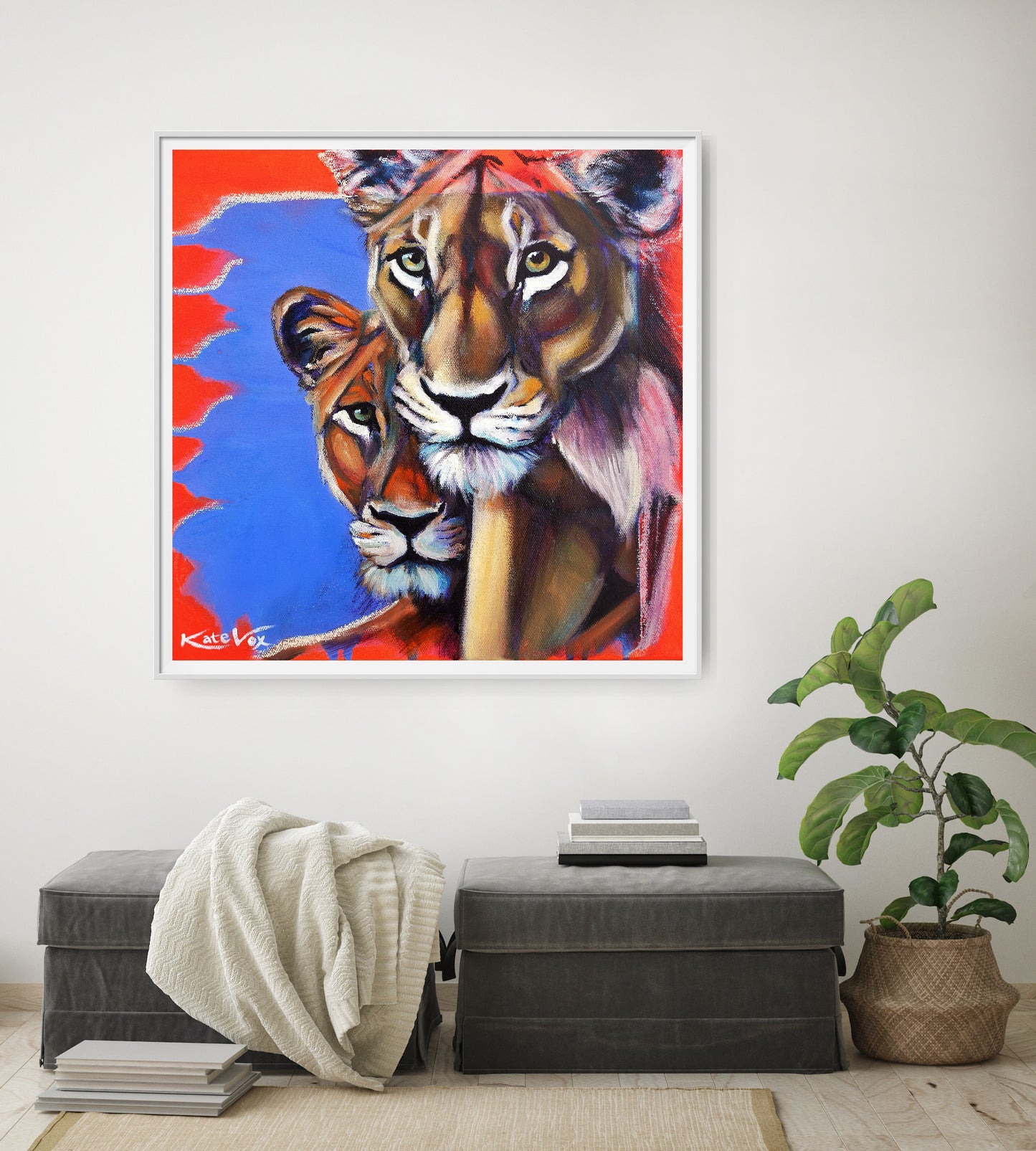 Framed artwork of two lions on a wall above a gray ottoman with a plant to the right.